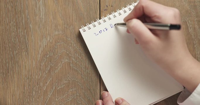 female teen writes 2017 resolutions on blank notepad