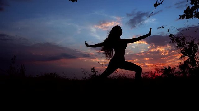 Silhouette Against Bright Color Sunset of One Young Graceful Girl Practicing Yoga Outdoors.