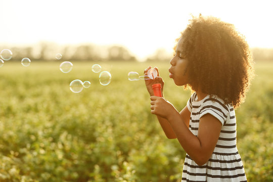 Little African American girl blowing bubbles in field