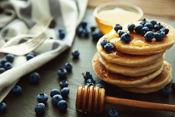 Stack of delicious pancakes with blueberries and honey on slate