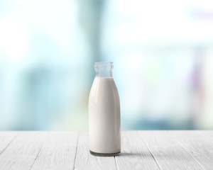 Glass bottle of milk on white wooden table against blurred background. Dairy concept.