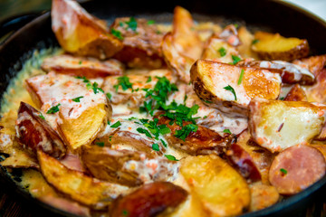 Oven baked potatoes with cream and cheese in black  in a frying pan on wooden table. Close up. Tasty food.