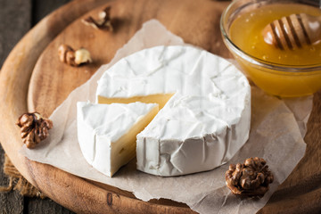 Brie type of cheese. Camembert cheese. Fresh Brie cheese and a slice on a wooden board with nuts,...