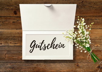 Gutschein - Text in Box mit Maiglöckchen auf rustikalem Holztisch