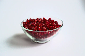 Pomegranate seeds in a clear bowl on a white background