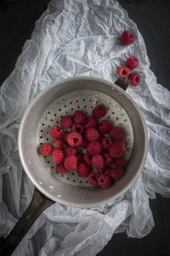 Raspberries in vintage colander on black slate background and wh