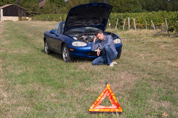 Close up on triangle warning sign with broken down car