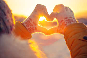 Woman hands in winter gloves Heart symbol shaped Lifestyle and Feelings concept with sunset light...