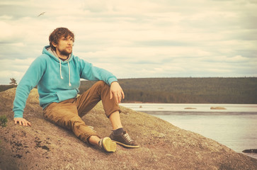 Young Man hipster relaxing alone outdoor with mountains and lake on background Lifestyle concept