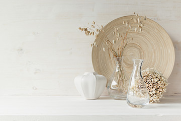 Soft home decor of  glass vase with spikelets and wooden plate on white wood background. Interior.