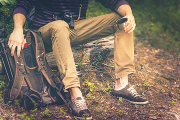 Traveler Man relaxing in forest with photo camera, backpack and thermos drinking tea Travel Lifestyle concept vacations outdoor