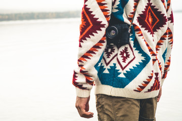 Man with retro photo camera Fashion Travel Lifestyle wearing knitted sweater clothing outdoor foggy nature on background