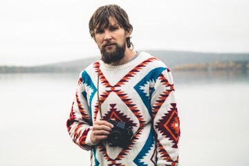 Young Man bearded with retro photo camera Fashion Travel Lifestyle wearing knitted sweater clothing outdoor foggy nature on background