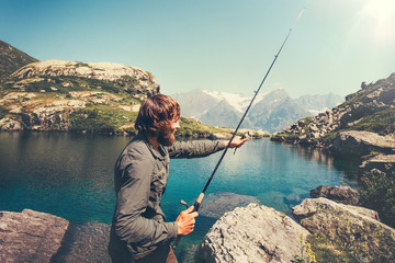Man Fisherman fishing with rod alone lake and mountains landscape on background Lifestyle Travel survival concept