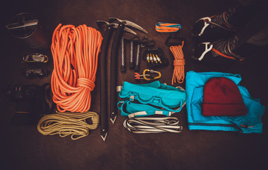 Climbing equipment set: orange rope, crampons, ice axe, shoes, harness and other set on dark...