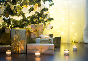 Tall christmas tree, beautifully decorated with balls, bows and lights. Lots of christmas gifts under the tree. Candles on wooden floor.