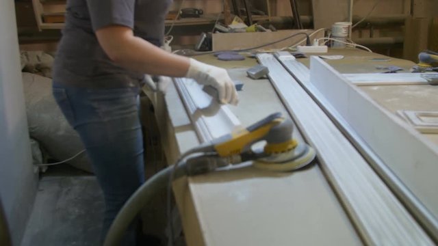 Female carpenter polishing board on the furniture factory