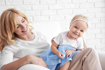 Mother with daughter sitting in armchair on white brick wall background