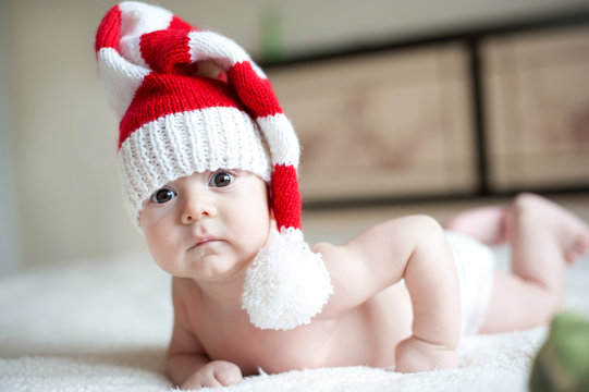 Christmas Cute Baby Boy/girl Lying On Red Soft Plaid Like On Snowdrift, Beautiful Funny Infant In Santa's Hat