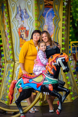Fototapeta na wymiar girl with mother and bubashka on roundabouts
