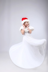 Full-length portrait of little girl in long white dress and Santa helper hat over light background