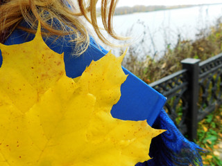 A girl walking on a shore holding a book and a bunch of maple leaves