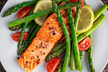 Fried salmon with asparagus, tomatoes, lemon, yellow lime on white plate