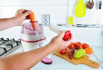 Closeup. Unrecognizable man presses carrot inside juicer to make tasty juice for breakfast from...