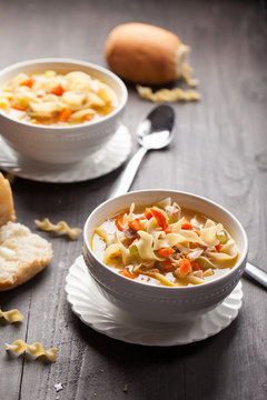 Homemade Turkey Noodle Soup with piping hot rolls on dark wood