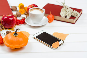 Autumn background, cup of cappuccino, mobile phone on wooden table.