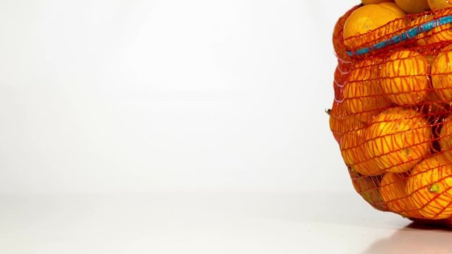 Slow motion of red sack of orange tangerines that falls down and fruits get out of it. On white background. 
