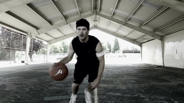 Man dribbles basketball up and down court and comes close up to camera for challenge.