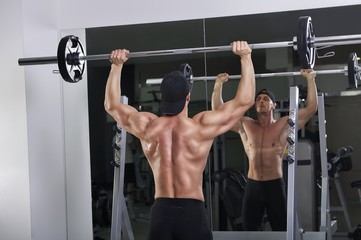 Naklejka premium Handsome powerful athletic man doing barbell shoulder press exercise. Strong bodybuilder with perfect muscles.
