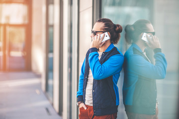 Young Man talking on his smartphone near glass of office building. Successful businessman in casual