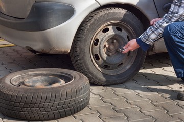 Man is changing winter tire with wheel wrench. Preparing the car for the winter. Repairing punctured tires.
