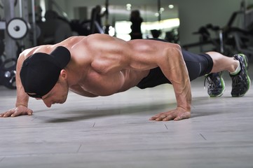 Handsome powerful athletic man performing push ups at the gym. Strong bodybuilder with perfect...