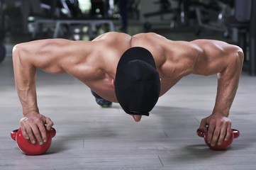 Handsome powerful athletic man performing push ups with kettle bell. Strong bodybuilder with  perfect shoulders, biceps and triceps.