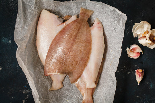 Four halves of raw megrim fish on baking paper over a black table, ready to be condimented and baked in oven. top view 