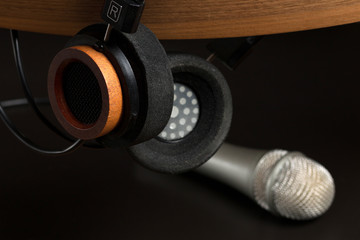Fashion headphones on a wooden stand and studio microphone on a black background. Music concept.