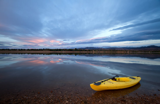 One Yellow Kayak with an oar on the shore of a lake at sunrise