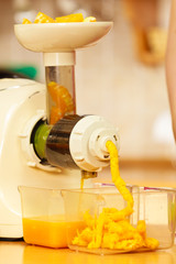 Making orange juice in juicer machine in kitchen