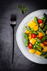 Vegetarian salad with asparagus, cherry tomatoes, bell pepper, slate background