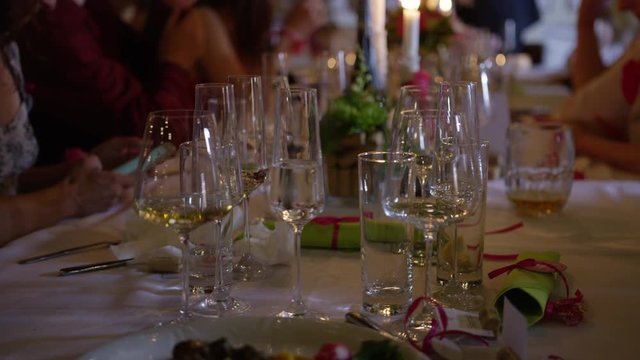 A wedding dinner table filled with glasses, while a woman uses her smart phone and people talk in the background. 4k.