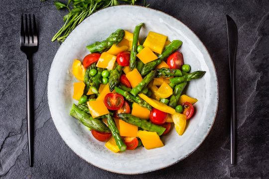 Vegetarian salad with asparagus, cherry tomatoes, bell pepper, slate background