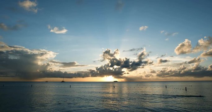 tropical sunset in the caribbean with cloudy skies and flat calm waters in a time lapse