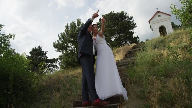 A newly married couple holds each other and point into the distance while posing for photos on stairs. 4k. In slow motion.