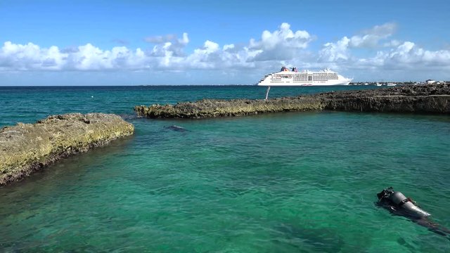 divers moving out from the beach to the ocean with a cruise ship in the background