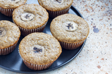 Freshly baked homemade banana cinnamon muffins with slice of banana on top, on the tray, copy space