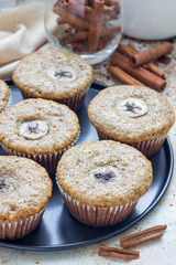 Freshly baked homemade banana cinnamon muffins with slice of banana on top, on the tray