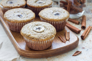 Freshly baked homemade banana cinnamon muffins with slice of banana on top, on wooden board, horizontal